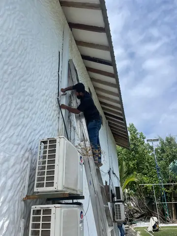 Technician on a ladder running cable along a building exterior